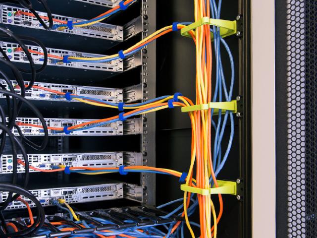 Indvendigt billede af et Enoc serverrack med monteret kabel management med farvekodede netværkskabler i blå, orange og sorte farver, organiseret med velcrobånd og tilsluttet netværksudstyr.