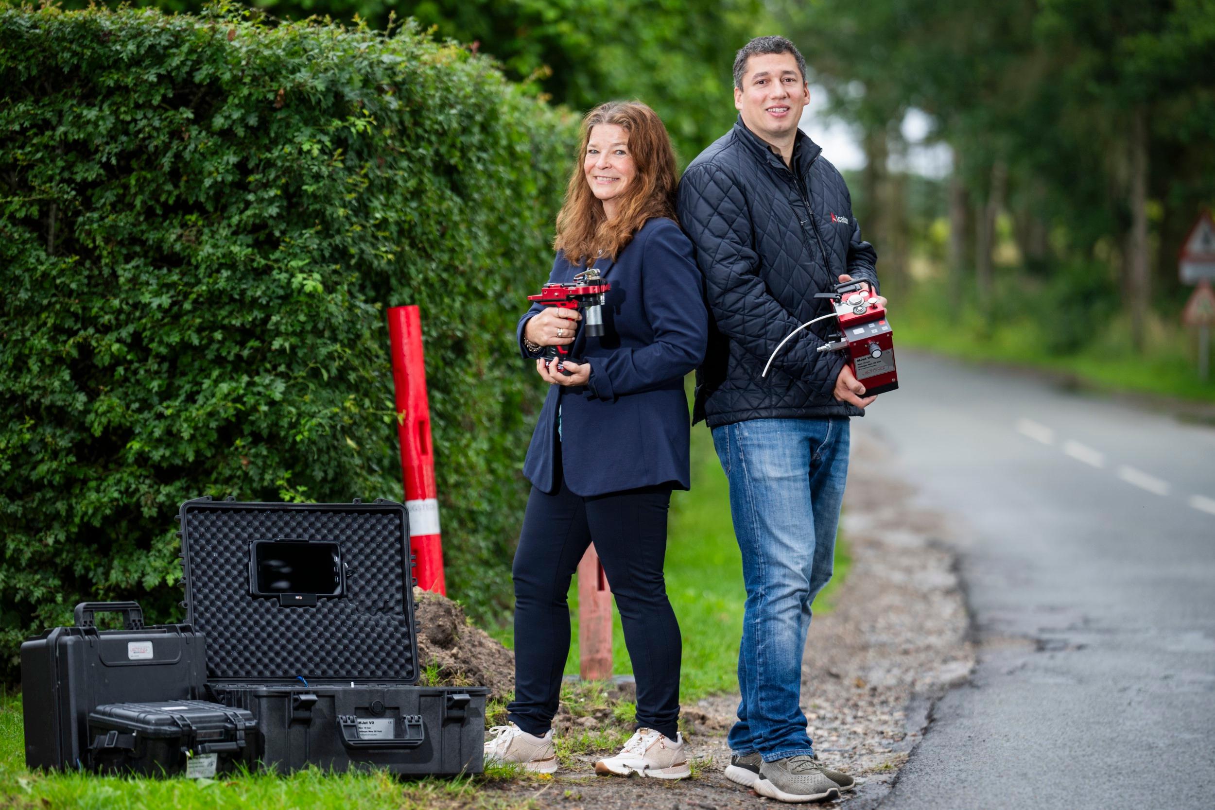Brian jensen fra Alcadon ved vejside med Jetting blæsemaskine i armene. På jorden står transportkufferter på græsset.