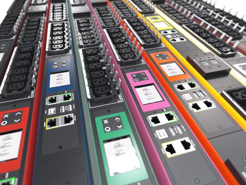 Nærbillede af farvekodede Raritan PDU-enheder (Power Distribution Units) med netværksporte, skærme og strømudtag, opstillet side om side til brug i datacentre og tekniske installationer.