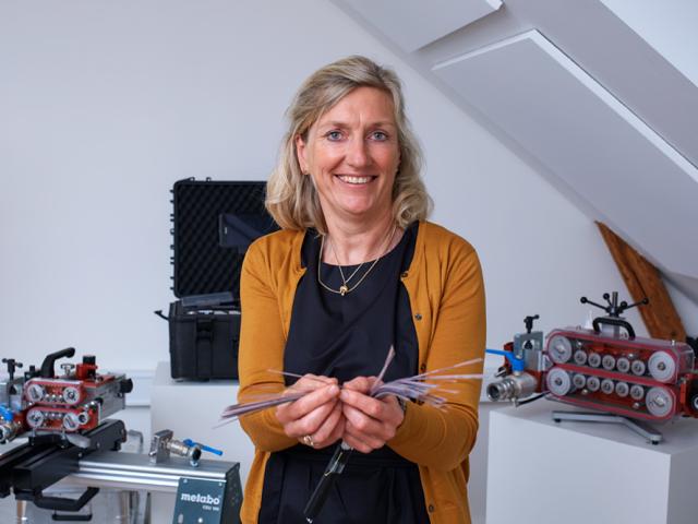 Susanne Stengade fra Alcadon viser fiberkabler fra OFS. I baggrunden ses flere fiberblæsemaskiner og teknisk udstyr på borde.